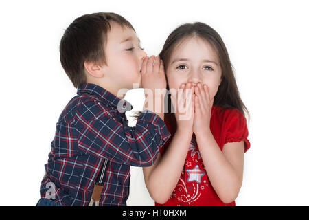 Little boy whispering funny story in a girl`s ear. She is smiling and covering her mouth with her hands. Isolated on a white background. Stock Photo